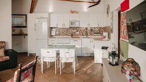 Una cocina compacta con armarios blancos, salpicadero de azulejos y un comedor con mesa de mármol y sillas blancas.