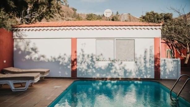 Una piscina con sillones de descanso y un pequeño edificio con techo de tejas.