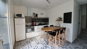 Een compacte keuken met een magnetron, oven en koffiezetapparaat, een eettafel met stoelen en vloertegels met een patroon.