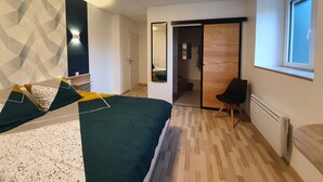 Een moderne slaapkamer met een bed, een stoel, een kledingkast en een badkamer zichtbaar door een geopende deur.