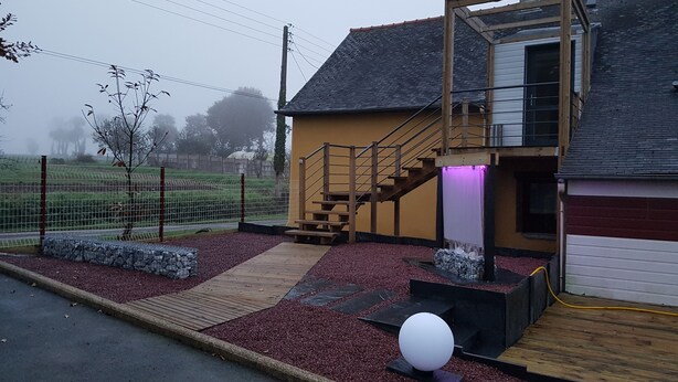 Een huis met een houten trap naar een balkon, een omheinde tuin en een grindpad.