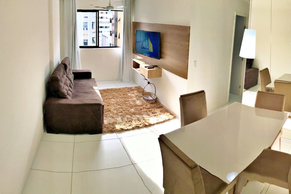 A modern living room with a sofa, a TV, a dining table, and chairs.