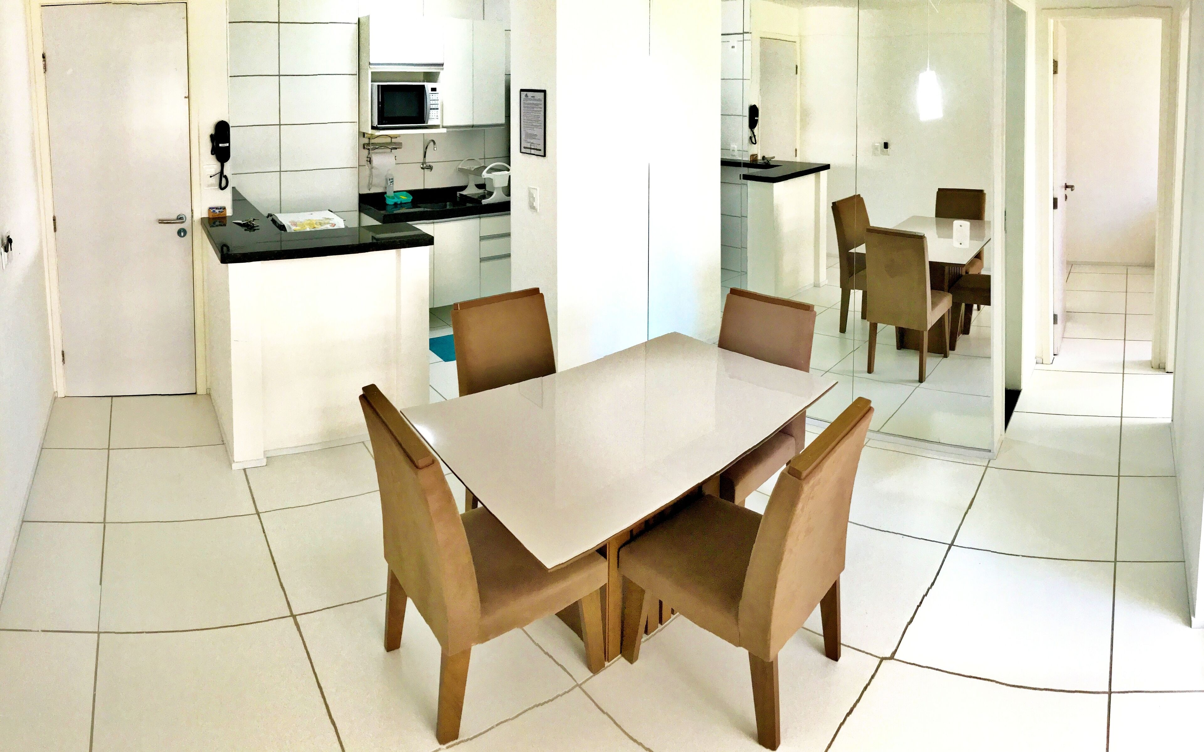 Una cocina moderna con microondas, lavamanos y armarios, un comedor con mesa y sillas, y un pasillo que lleva a otra habitación.
