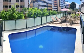 A rooftop swimming pool with a glass balustrade, lounge chairs, and umbrellas. - Vacanze - Golden Place (Maceió)