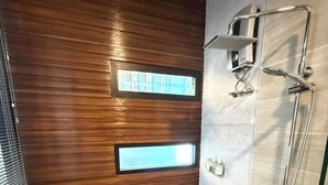Un baño moderno con pared de paneles de madera, cabina de ducha con mampara de vidrio y tocador de madera con toallas.