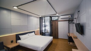 Una habitación de hotel moderna con una cama grande, mesitas de noche, un escritorio, un televisor y un equipo de aire acondicionado.