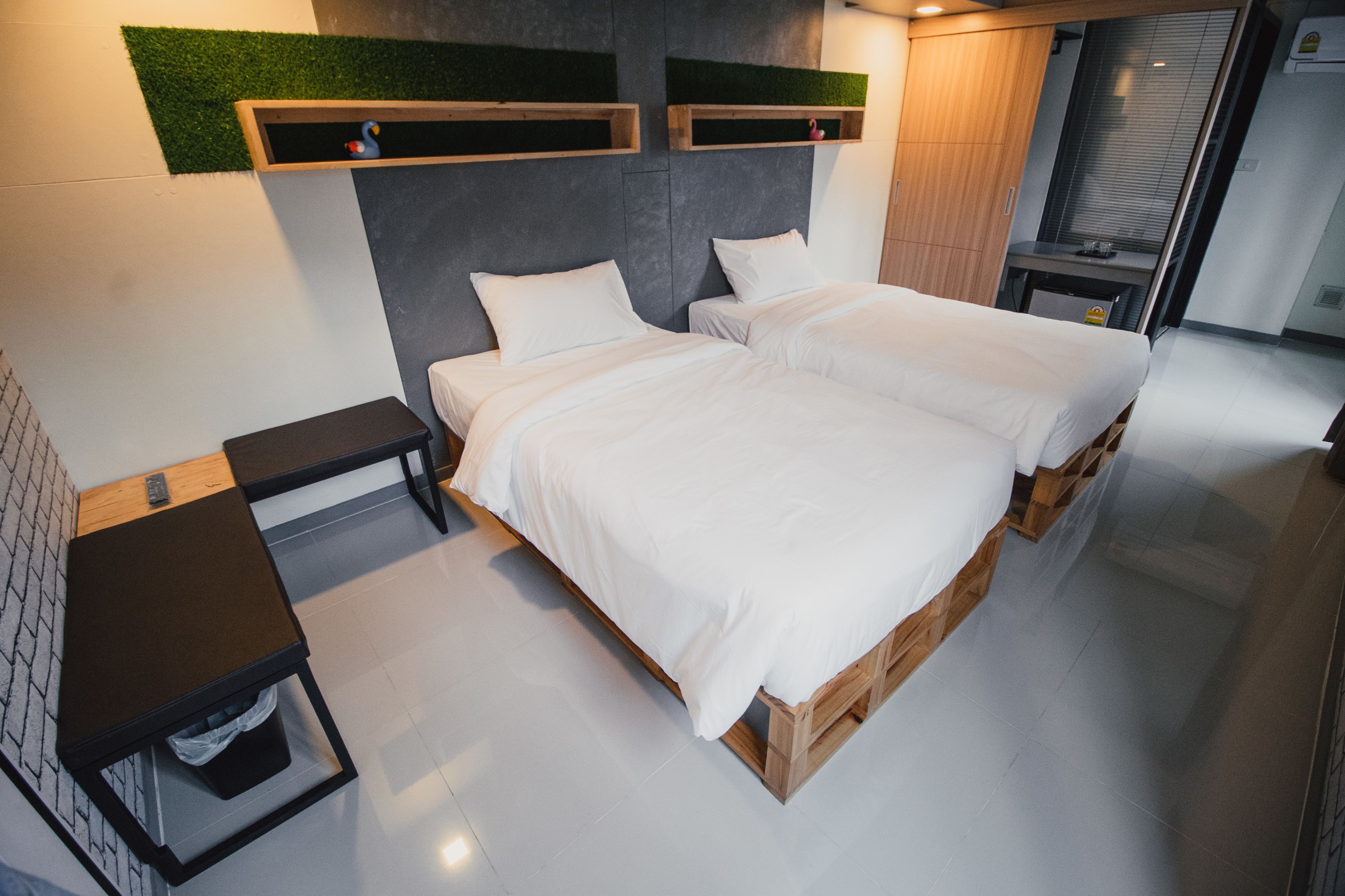 A modern hotel room with two beds, a small table, and a trash bin.