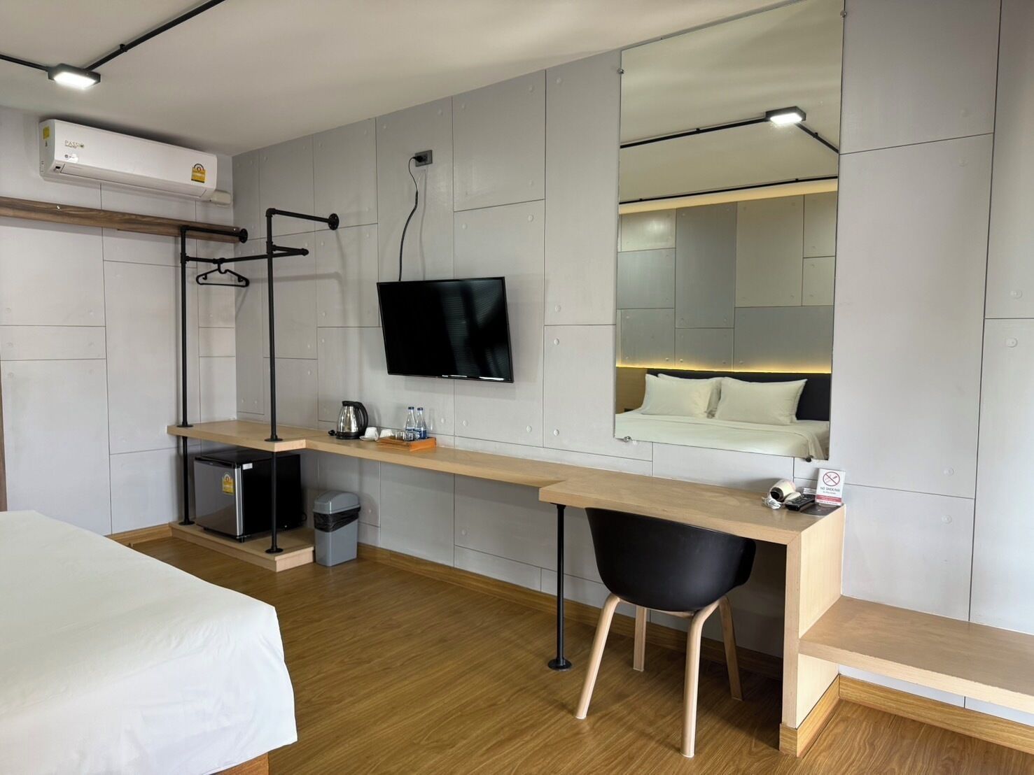 A modern hotel room with a bed, desk, chair, TV, and a mirror.
