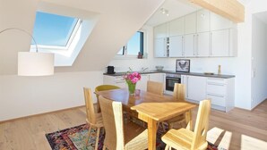 A modern kitchen with white cabinets, a wooden dining table, and a skylight. - Landhotel Herzberger (Scheidegg)
