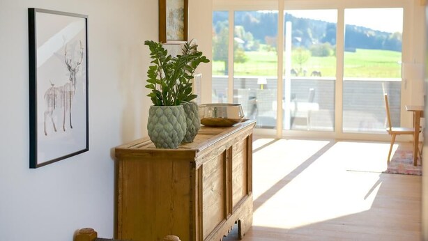 A room with a wooden cabinet, a framed deer artwork, and a potted plant. - Landhotel Herzberger (Scheidegg)