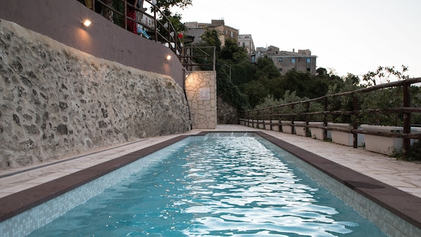 A swimming pool with a stone wall on one side and a wooden fence on the other. - Splendid receptive structure, new construction, anti-seismic. (Ragusa)
