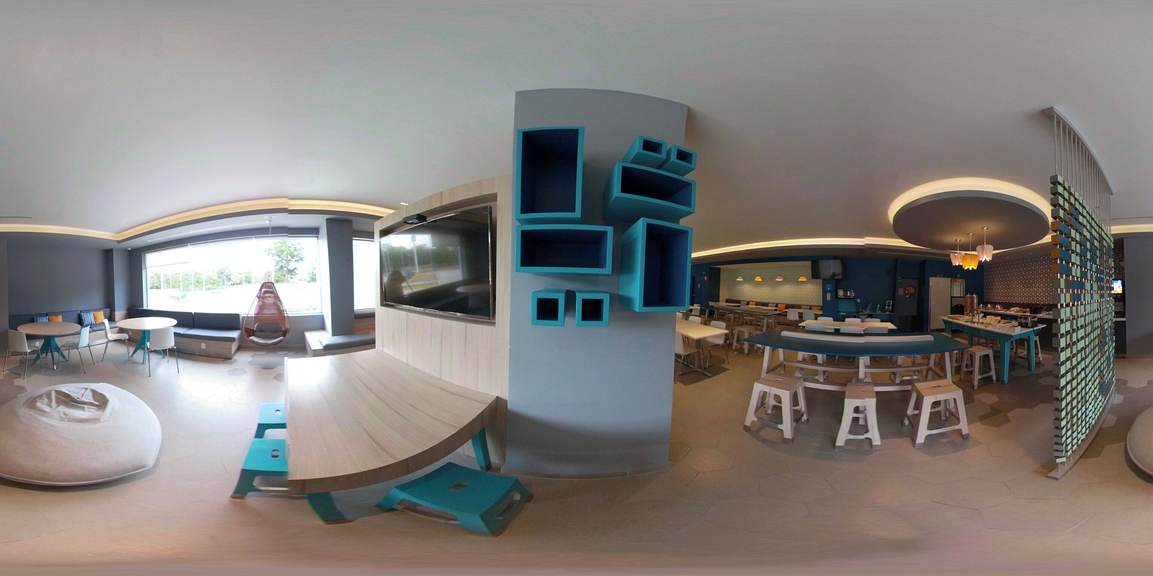 A modern interior with a large curved table, seating areas, and a TV screen.
