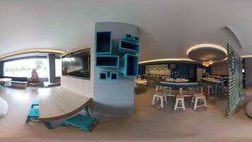 A modern interior with a large curved table, seating areas, and a TV screen.