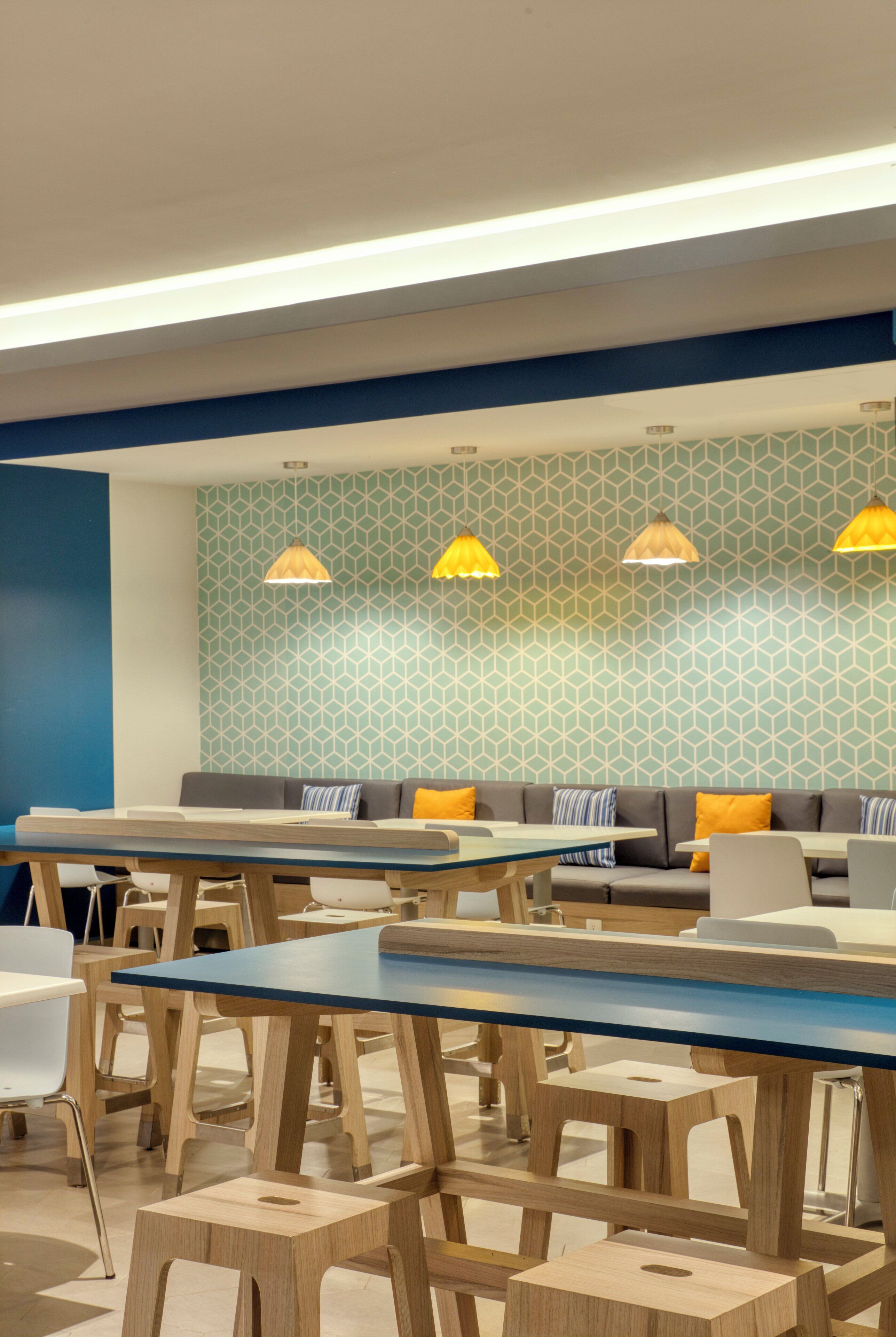 A modern dining area with wooden tables and chairs, a blue accent wall, and patterned wallpaper.