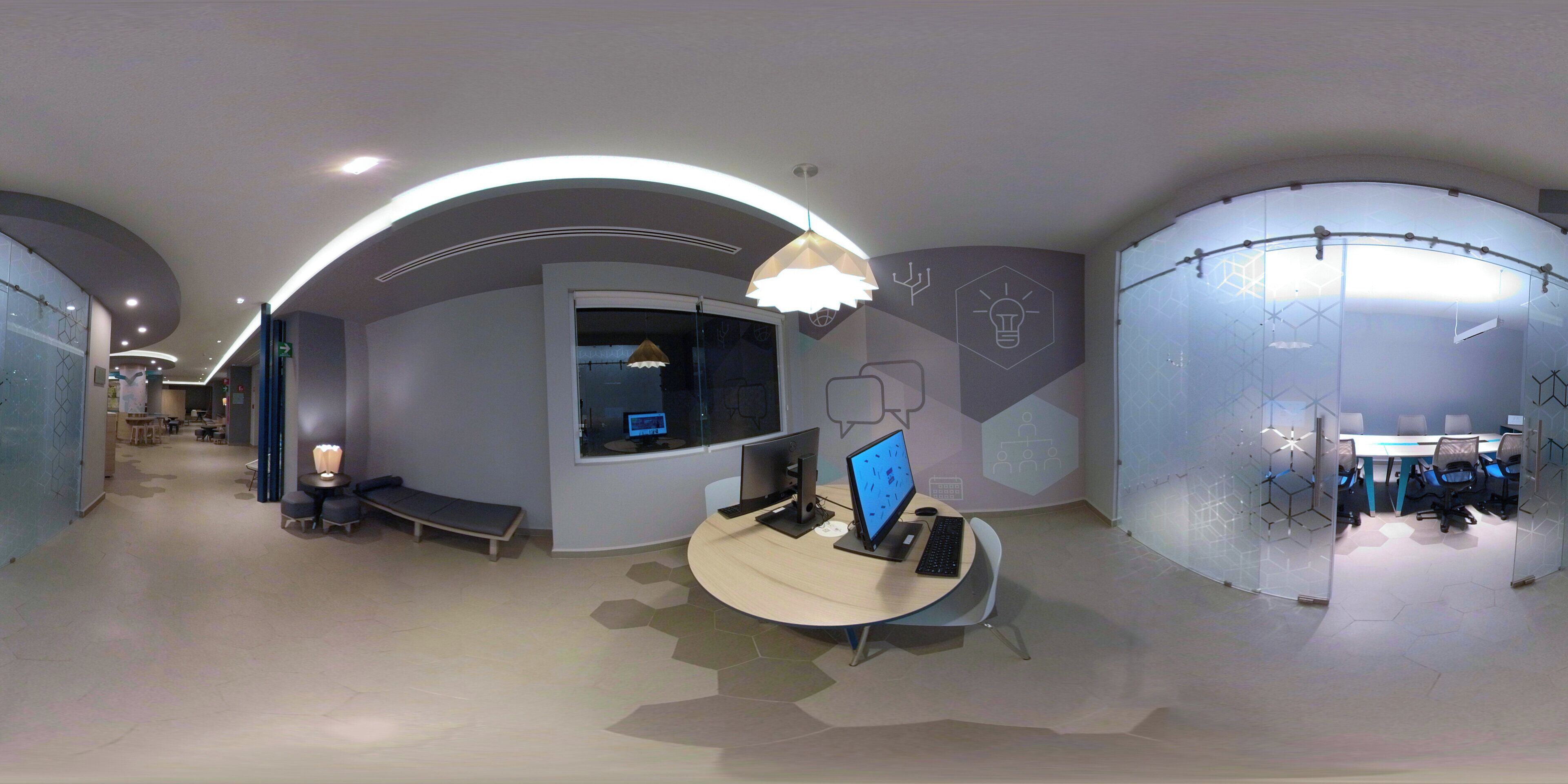 A modern office space with curved ceilings, a central desk area with computers, and a meeting room visible through a glass partition.