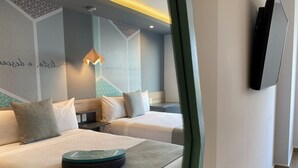 A modern hotel room with two beds, a small desk, and a mounted TV.