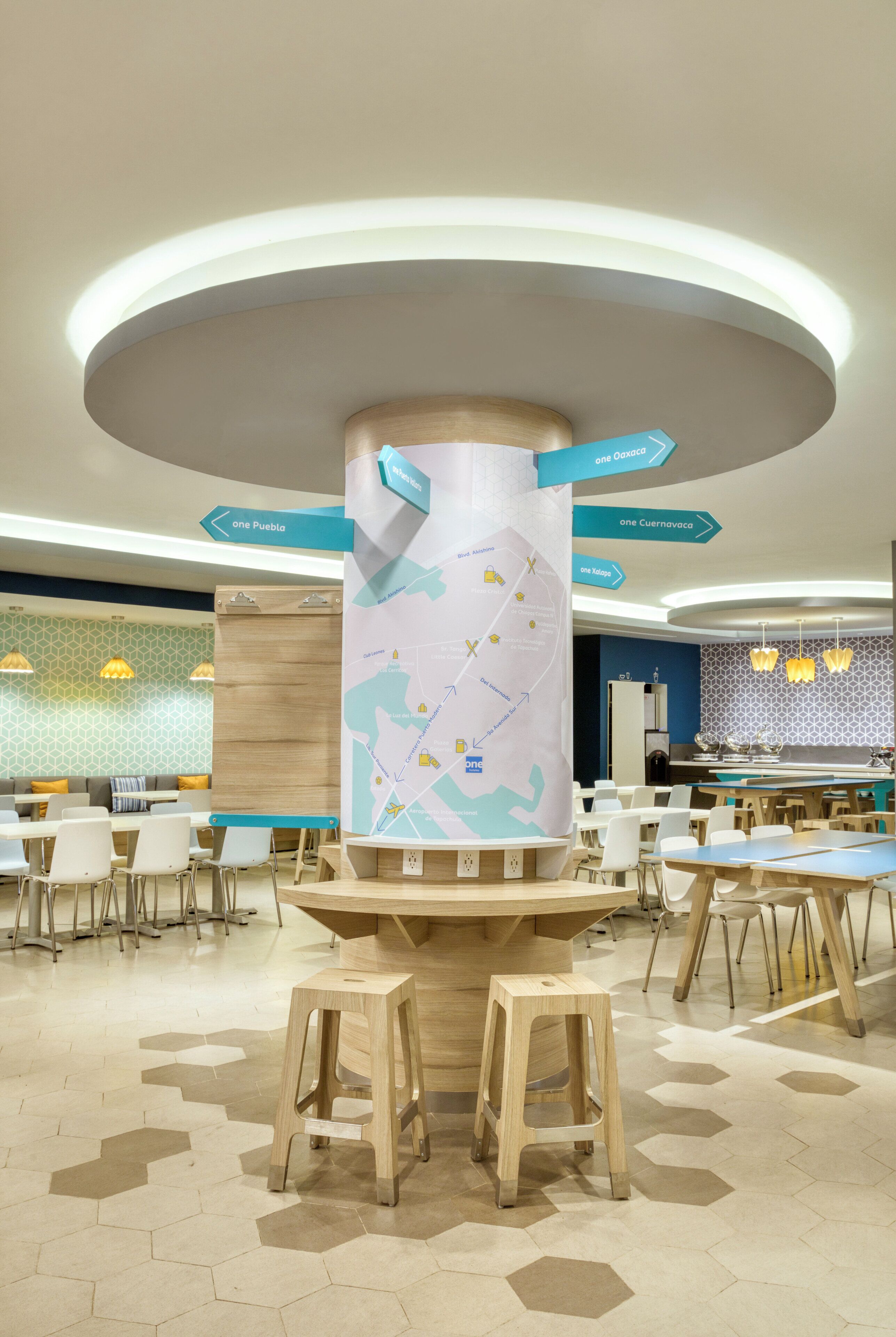 Un espace repas moderne avec un sol à motifs hexagonaux, des tabourets en bois et des panneaux de signalisation.