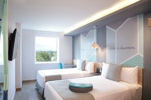 A hotel room with two beds, a window, a desk, and a view of greenery. - One Tapachula (Tapachula)