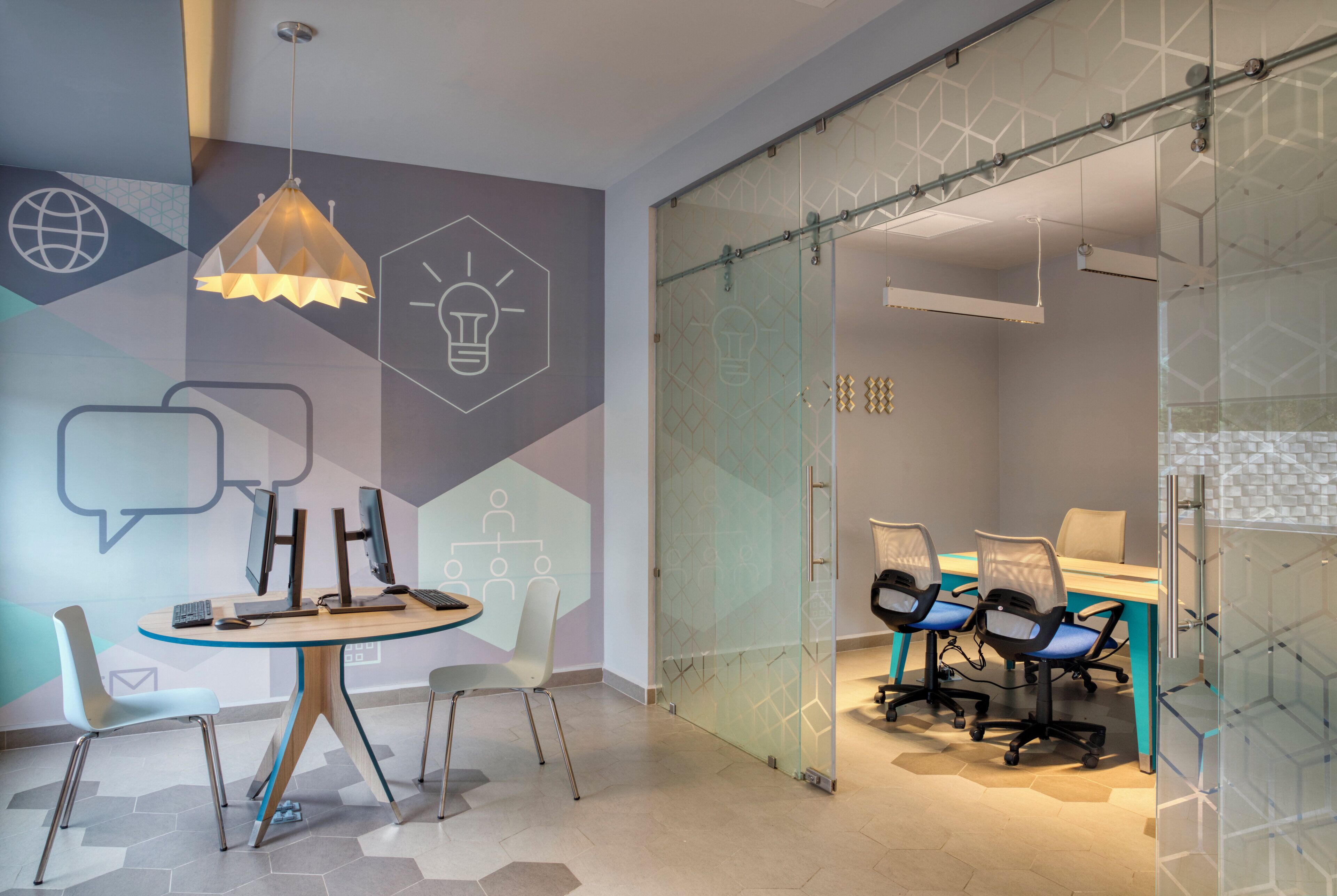 A modern meeting room with a glass partition, a round table with chairs, and a light fixture on the ceiling.