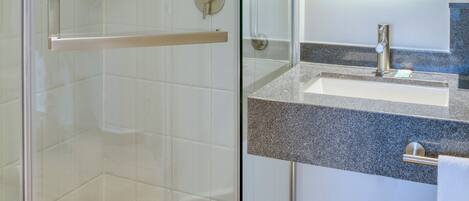 Un baño moderno con cabina de ducha de vidrio, lavamanos con encimera de granito y un espejo grande.