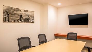 A conference room with a long table, four chairs, a flat-screen TV, and a cityscape painting on the wall.