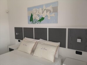 A bedroom with a bed, two nightstands, a wall-mounted artwork, and a headboard with a panel design. - B&B Corallo (Alliste)