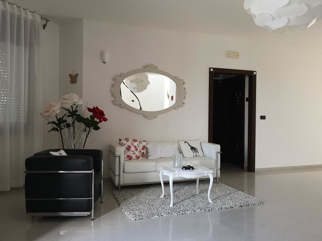 Una sala de estar moderna con un sofá blanco, un reposapiés negro, una mesa de centro blanca y un espejo en la pared.