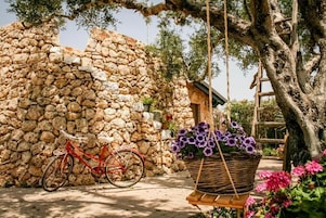 Un muro de piedra, una bicicleta roja y una cesta de flores moradas.