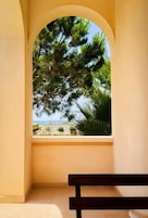 Una habitación con vista a una playa y árboles, a través de un ventanal arqueado.