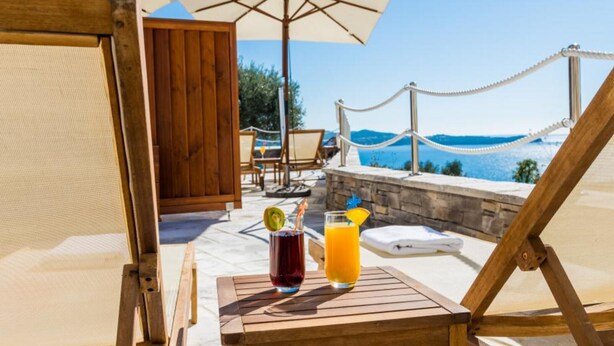 A wooden lounge chair with a table, a drink, and an umbrella.