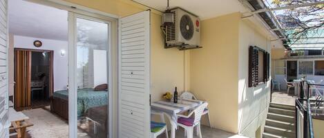 Un balcón con puerta corredera de vidrio que da a un dormitorio, una mesa con sillas y un equipo de aire acondicionado instalado en la pared.