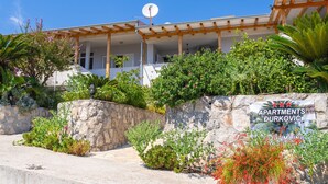 Un edificio con un muro de piedra, un letrero para apartamentos y abundante vegetación.