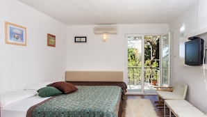 Un dormitorio con cama, televisor, una silla y un balcón con vistas a la vegetación.