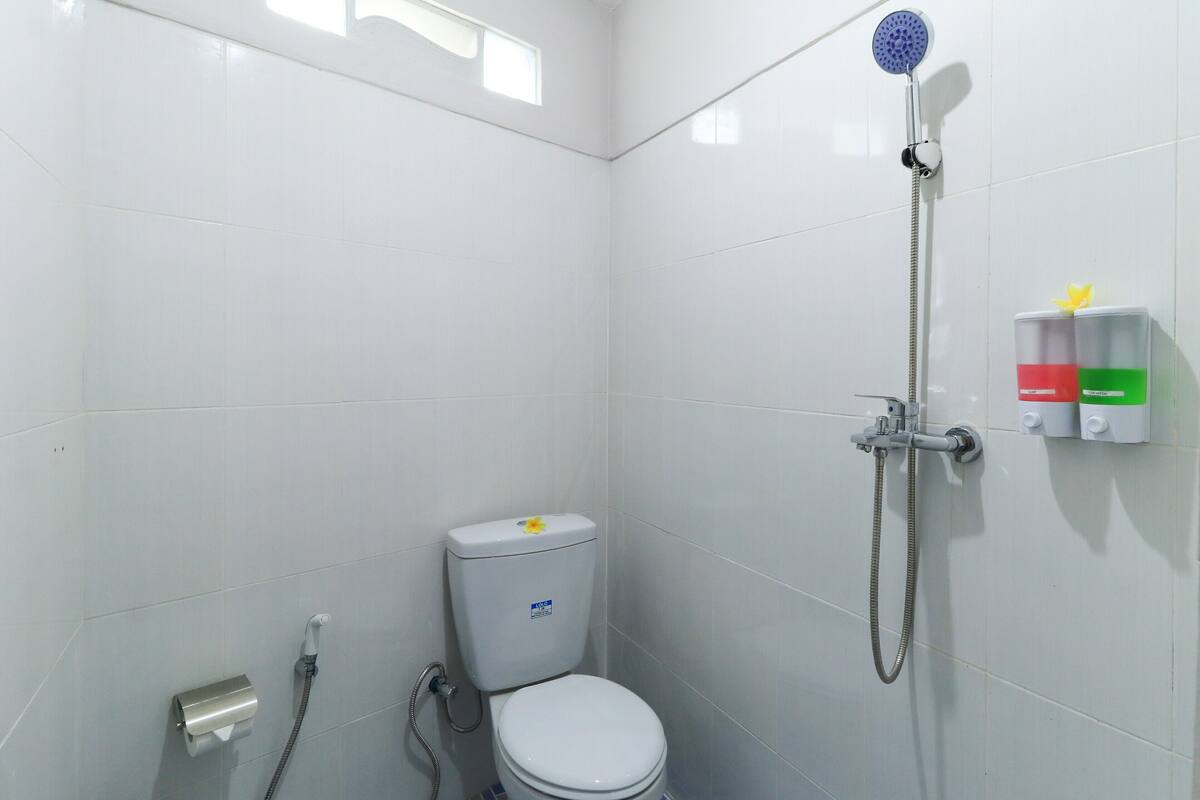 Een kleine badkamer met witte tegels, voorzien van toilet, een handdouche en een zeepdispenser aan de muur.