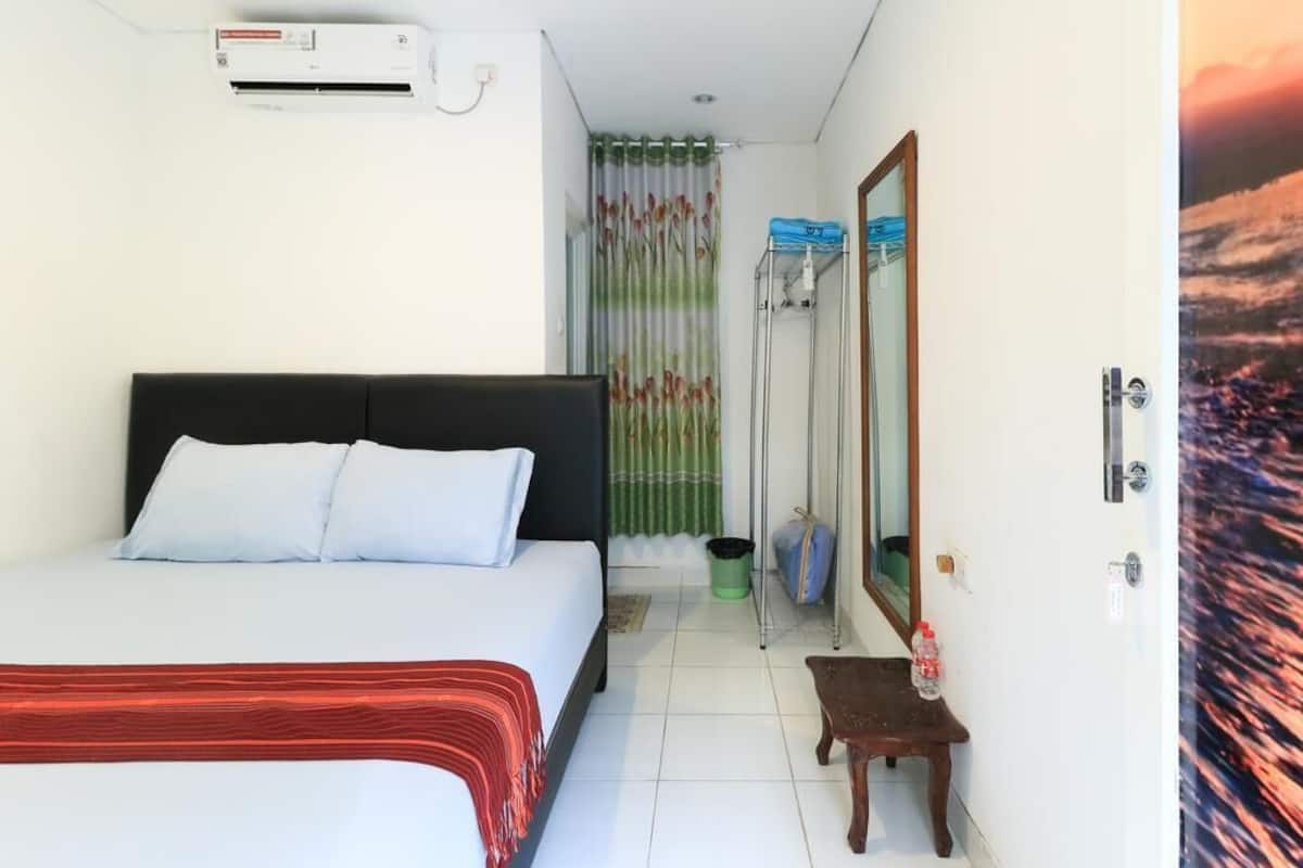 A hotel room with a bed, air conditioning unit, a mirror, a small table, and a curtain with a floral pattern.