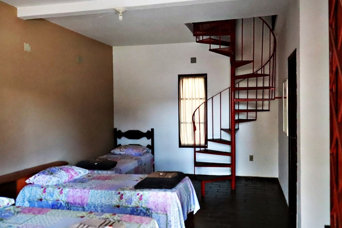 Una habitación con dos camas, una ventana con cortinas y una escalera espiral roja.