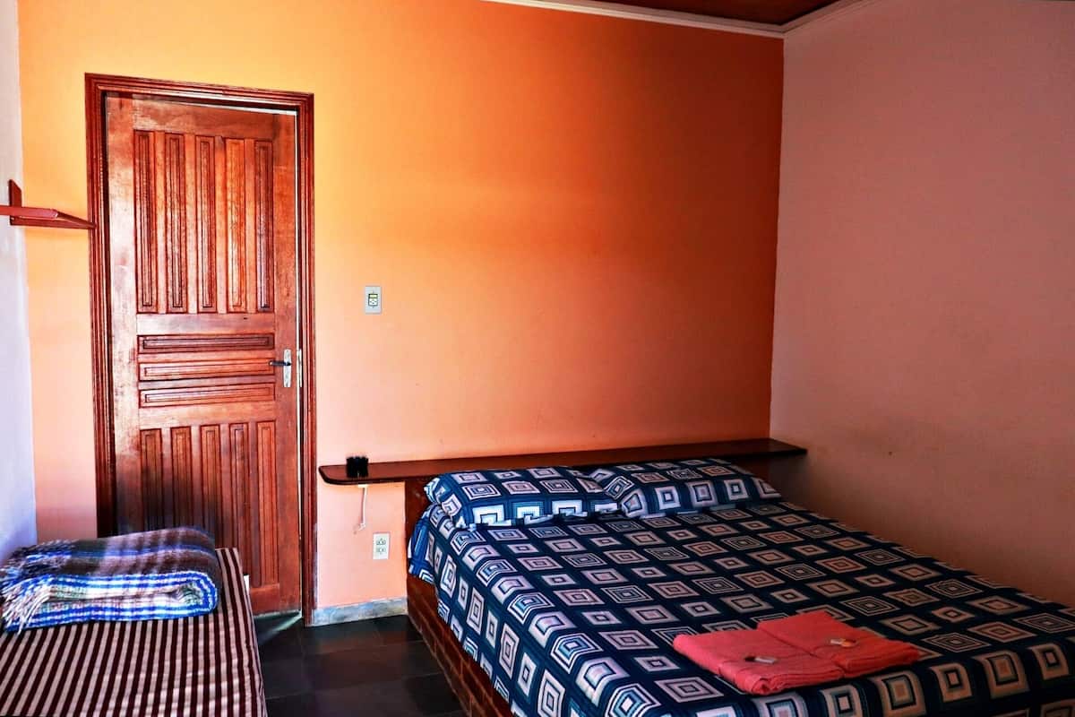 Una habitación pequeña con una cama individual, una puerta de madera y una mesita.