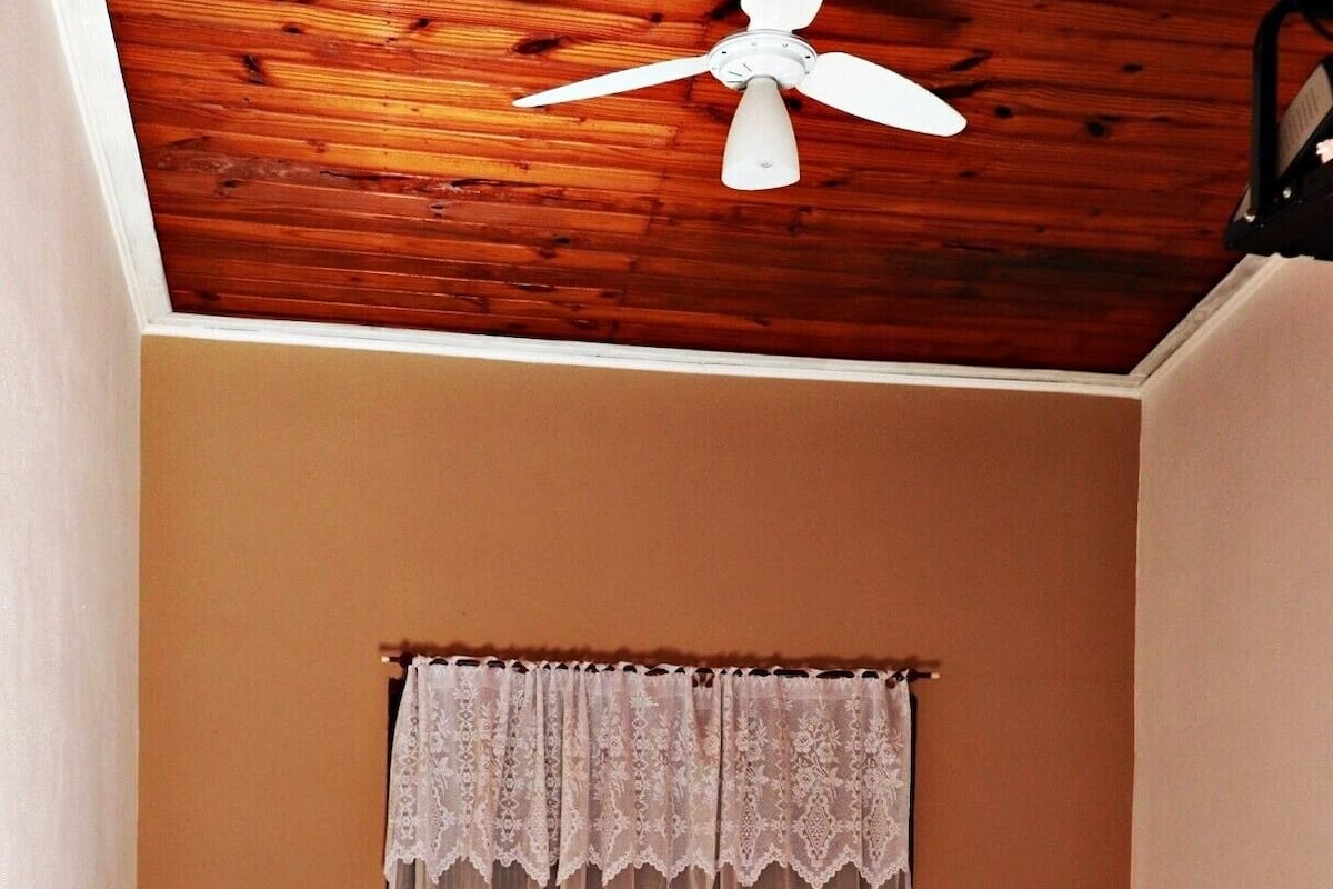 Una habitación pequeña con dos camas individuales, techo de madera y una ventana con cortina de encaje.