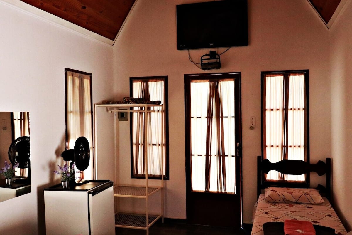 Un dormitorio con literas, un escritorio con silla, un televisor montado en la pared y ventanas amplias con cortinas.