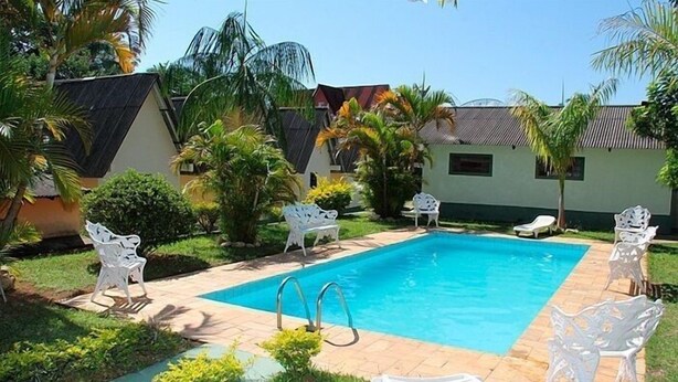 Una piscina rectangular con solárium de azulejos, rodeada de sillas de plástico blancas y palmeras.