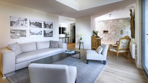 Uma sala de estar moderna com um sofá, poltronas e uma mesa de centro. Há quadros nas paredes e uma parede de pedra rústica ao fundo.