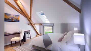 A bedroom with a sloped ceiling, a bed with pillows, a desk with a chair, a radiator, and a skylight.
