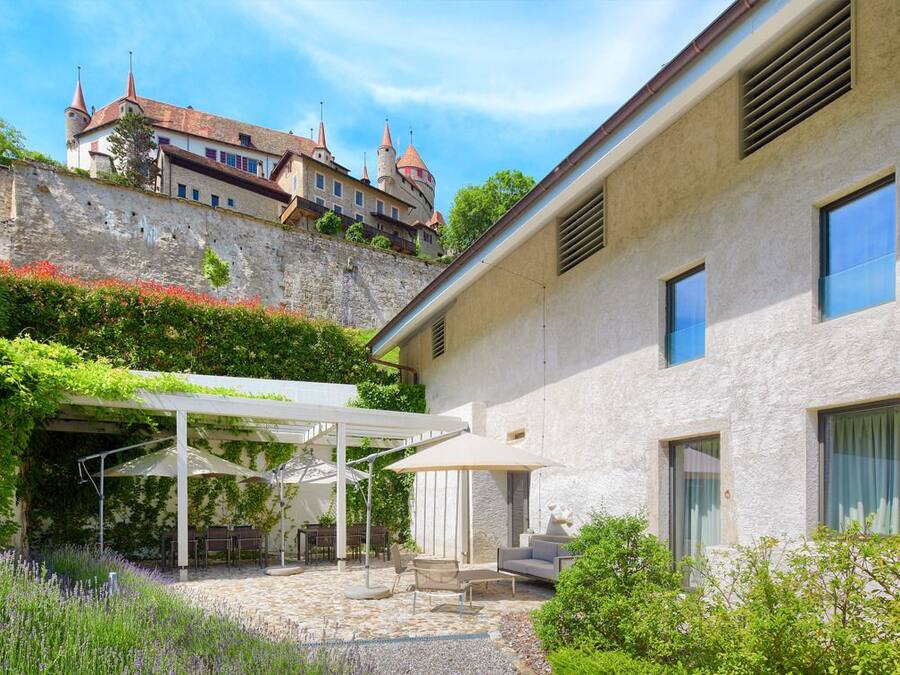 A courtyard with outdoor seating, a stone wall, and a building with a tower.