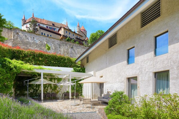 Une cour avec des sièges en plein air, un mur en pierre et un bâtiment doté d’une tour.