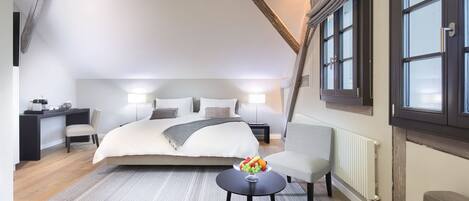 A bedroom with a large bed, a desk, a chair, and a small table with fruit.