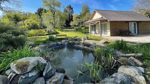 A house with a wooden deck, a pond, and a bench.
