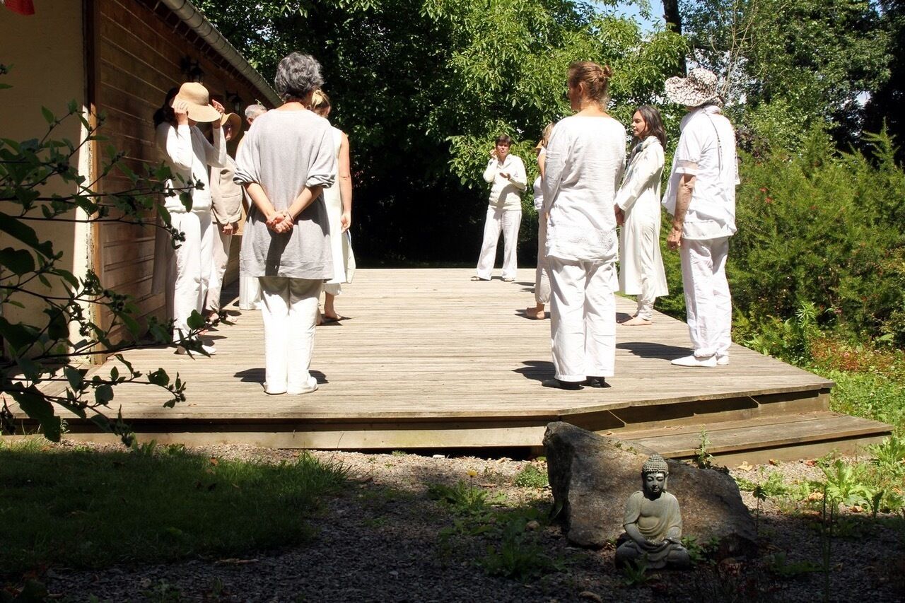 Un grupo de personas vestidas de blanco sobre una plataforma de madera al aire libre, rodeado de follaje.