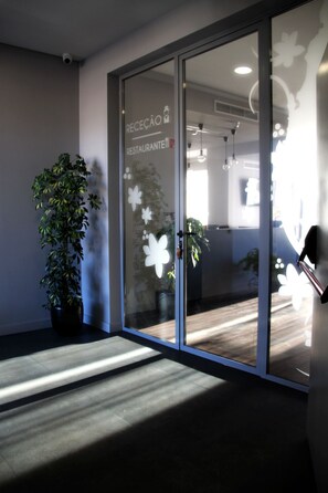 A reception area with a glass door, a potted plant, and a sign indicating a restaurant. - Basto Vila Hotel (Cabeceiras de Basto)