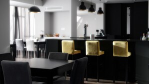 A modern dining area with a black and gold color scheme, featuring a long table and several chairs, a bar area with a counter, and pendant lighting. - Basto Vila Hotel (Cabeceiras de Basto)