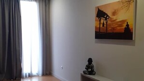 A spacious living room with a wooden floor, a large window with curtains, a wall-mounted painting, and a built-in shelf with a statue. - Basto Vila Hotel (Cabeceiras de Basto)